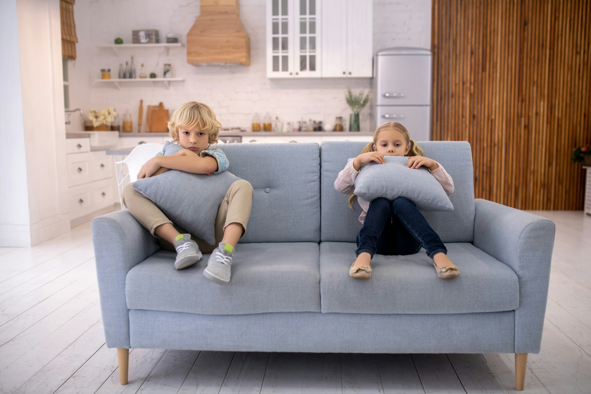 Blond kids sitting on the sofa and looking angry